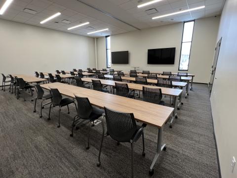 A large meeting room with tables and chairs for fourty and two large televsions. 