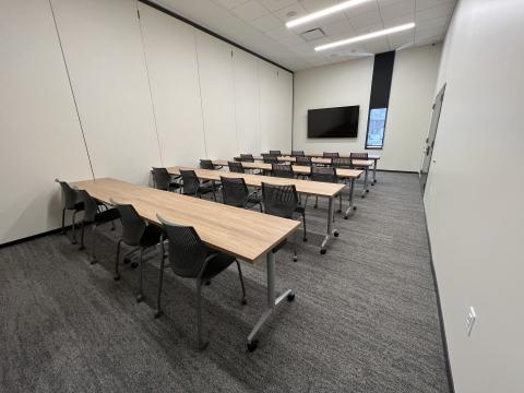 A room set up with 5 rows of chairs and 4 chairs per row. There is a TV at the front of the room.