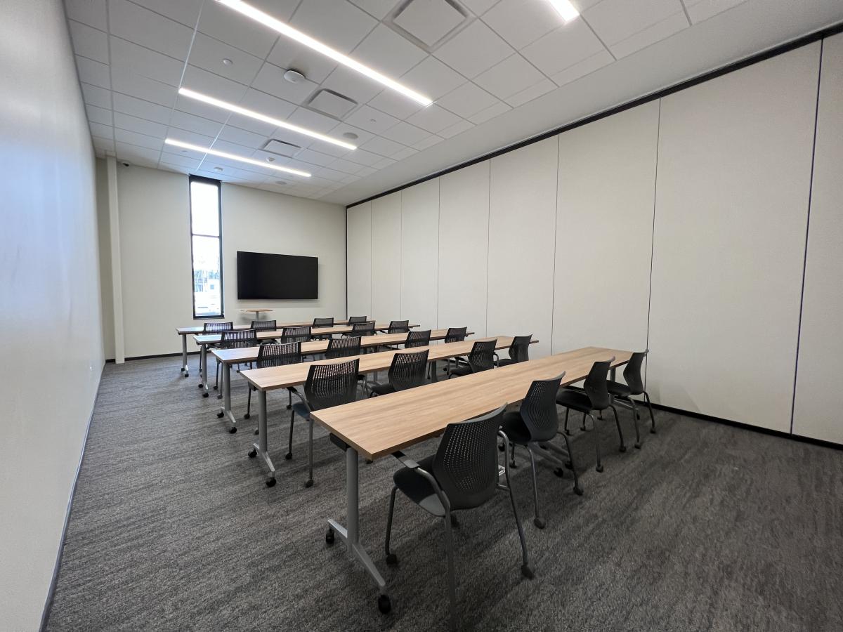 A room set up with 5 rows of chairs and 4 chairs per row. There is a TV at the front of the room.